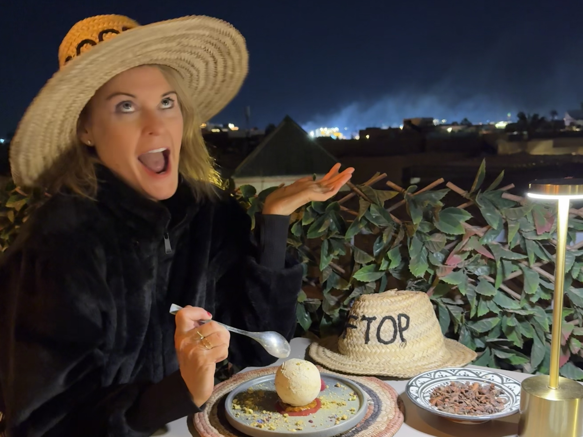 Woman with a straw hat at night eating desert pulling a funny face at M heritage 